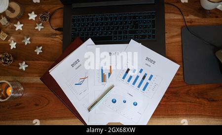 Top view of documents and report papers with graphs and charts lying on laptop computer on a christmas holiday decorated desk. Stock Photo