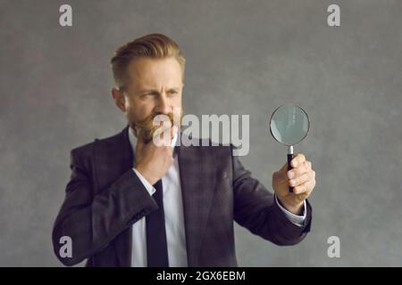 Serious pensive thoughtful man businessman looking through magnifying glass Stock Photo