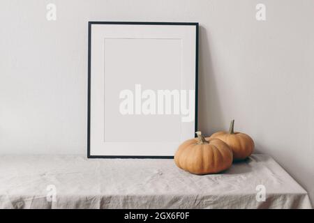 Autumn still life. Vertical black picture frame mockup. Pale orange pumpkins on linen table cloth. White wall background. Minimal rustic interior Stock Photo
