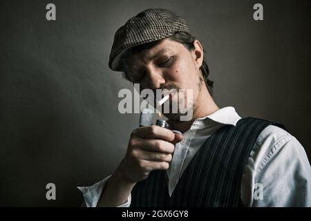 Young guy lights a cigarette, blows smoke, dressed in a retro style, in a beret, cinematic shot, big closeup Stock Photo