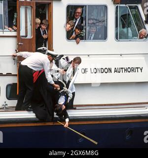 Close up historical 1990s archive view of the old custom & tradition of Beating the Bounds carried out in 1992 by church of All Hallows by the Tower with help from church clergy and boys from St Dunstan’s College school & staff assisted by PLA crew in holding a boy upside down  by rope from a 90s Port of London Authority launch to beat the south boundary in river water with a cane an unusual event in the middle of River Thames an archival image in the City of London England UK Stock Photo