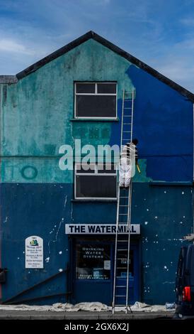 Painting the building blue. A man on a ladder painting a building a deep shade of blue. Stock Photo