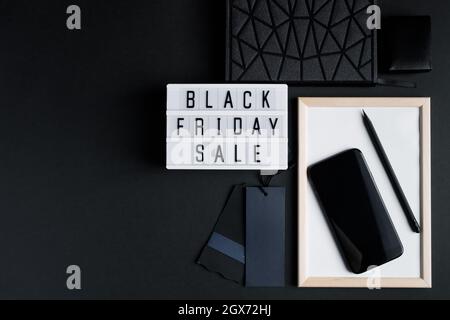 Black Friday online sale concept. Monochromatic flatlay on a dark background. Smartphone and accessories. Stock Photo