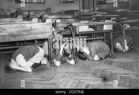 These London schoolchildren in an air raid drill as a precaution in case an air raid comes too fast to give them a chance to leave the building on July 20, 1940. They were told to go to the middle of the room, away from windows, and hold their hands over the backs of their necks. Stock Photo