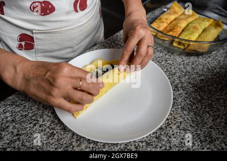 Woman in an apron rolling delicious homemade Cannelloni filled with spinach and ham Stock Photo