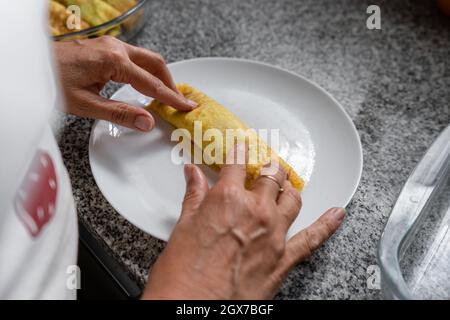 Woman in an apron rolling the stuffed pancake for preparing delicious homemade Cannelloni Stock Photo