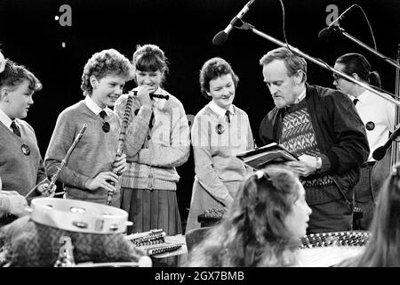 Richard Stilgoe, OBE, English songwriter, lyricist and musician, talking with young musicians during a rehearsal of the Schools Prom at the Royal Albert Hall, London,  in 1987.