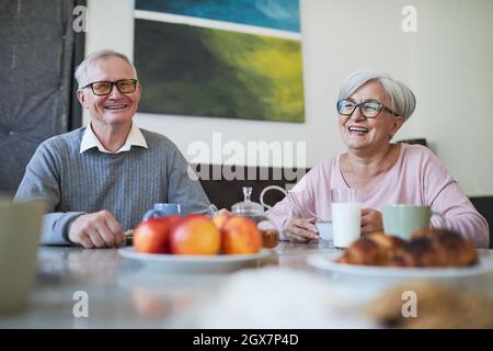 Couple of smiling senior people enjoying breakfast at dining table in nursing home, copy space Stock Photo