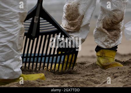 Huntington Beach, California, USA. 4th Oct, 2021. Workers in protective suits clean up an area of the beach after a major oil spill dumped 126,000-gallon oil from an offshore oil platform. A massive oil spill off the Orange County coast in Southern California prompted the closure of a 9-kilometer long beachfront area and crews from the California Department of Fish and Wildlife (CDFW) are cleaning up the pollution from facilities in federal waters. (Credit Image: © Jason Ryan/ZUMA Press Wire Service) Stock Photo