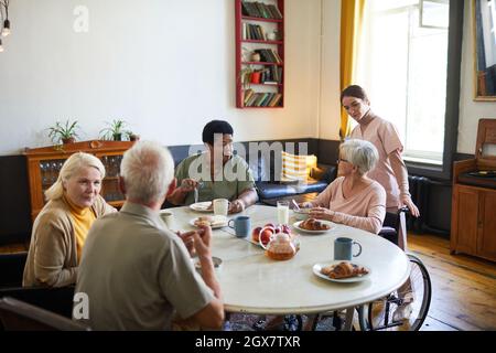 Warm-toned portrait of diverse group of senior people enjoying breakfast in cozy nursing home, copy space Stock Photo