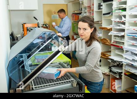 Female worker packs notebooks in a vacuum packing Stock Photo