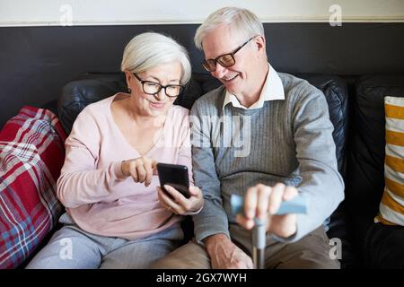 High angle portrait of smiling senior couple using smartphone in nursing home, copy space Stock Photo