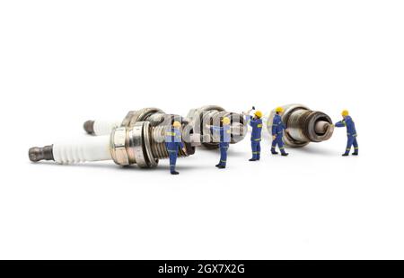 Miniature mechanic with old used engine spark plugs on white background. Stock Photo