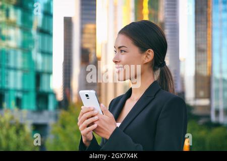 Phone young business woman Asian eurasian lady using mobile cellphone working in office outside background. Businesswoman commuting walking in city Stock Photo