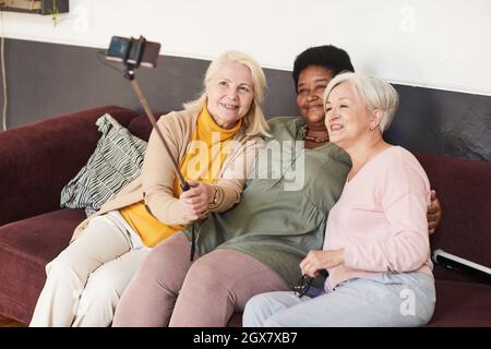 High angle portrait of three senior women taking selfie in nursing home using selfie stick Stock Photo