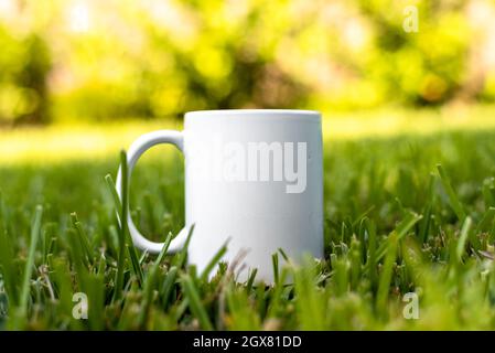 White porcelain mug cup isolated on green grass background with copy space. Mock up for design. Stock Photo