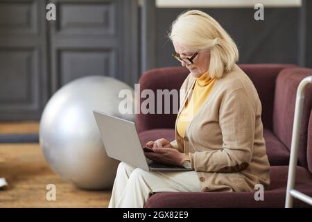 Side view portrait of elegant senior woman using laptop while relaxing in nursing home, copy space Stock Photo