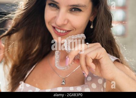 Beautiful caucasian woman holding transparent mouth guards for bite correction. Girl with silicone braces outdoors. Stock Photo