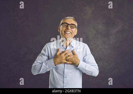 Happy grateful senior man smiling, holding hands on his chest and saying thank you Stock Photo