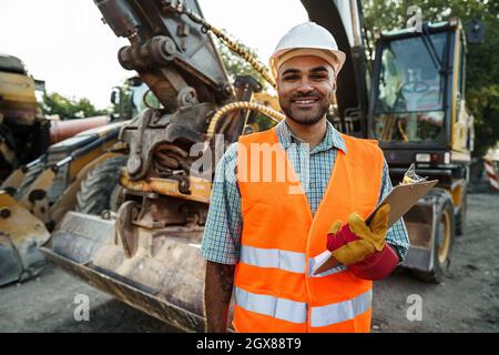 Young man engineer in workwear standing in construction site with clipboard Stock Photo