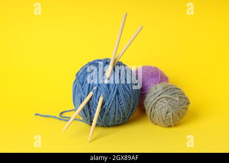 Multi-colored balls of yarn with knitting needles on yellow background. Stock Photo