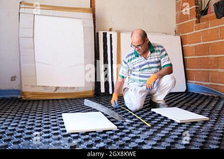 Worker measuring with tape before installing radiant floor system. Stock Photo