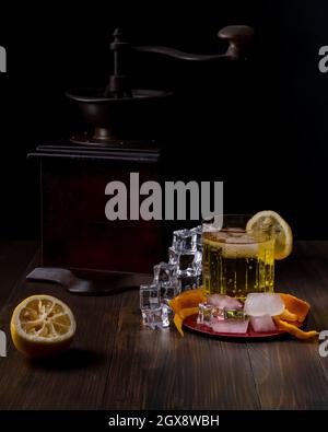 A glass of cedar carbonated soft drink with ice cubes on wooden table with lemon slice next to a coffee grinder on dark background Stock Photo