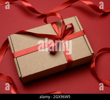 rectangular brown cardboard box tied with a silk red ribbon on a red background, top view, close up Stock Photo