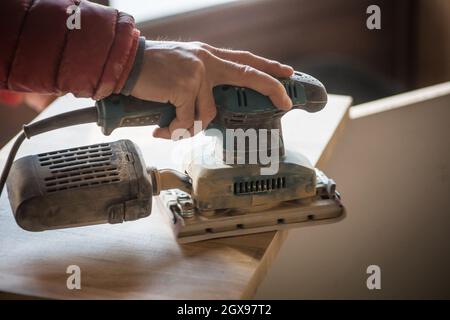 Man sanding wood plank using electric sand machine. Stock Photo