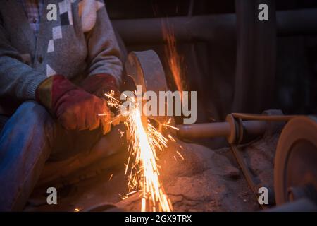 the blacksmith polishing metal products making sparks while using a grinding machine in his traditional workshop Stock Photo