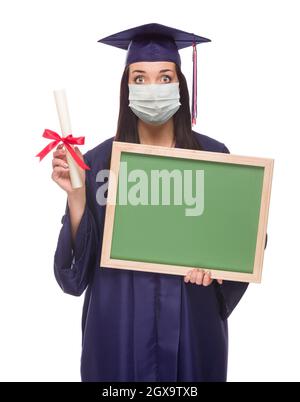 Graduating Female Wearing Medical Face Mask and Cap and Gown  Holding Blank Chalkboard Isolated on a White Background. Stock Photo