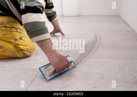 Grouting ceramic tiles. Tilers filling the space between ceramic wood effect tiles using a rubber trowel on the floor in new modern apartment Stock Photo