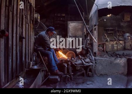 the blacksmith polishing metal products making sparks while using a grinding machine in his traditional workshop Stock Photo