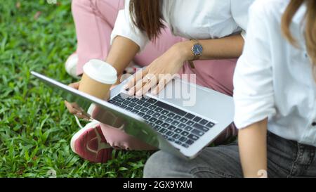 Cropped image of two attractive female college students sitting in a park using a laptop computer to discuss and collaborate on a project. Stock Photo