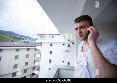 Painter making telephone call while standing on balcony during break from work  Decorator Using Mobile Phone Standing Outside Stock Photo