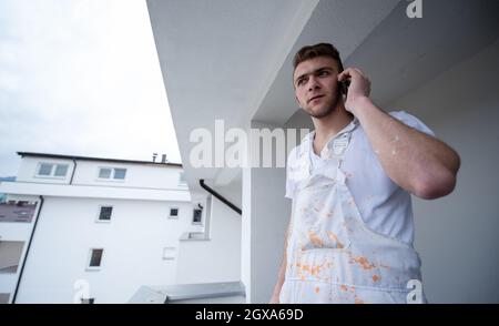 Painter making telephone call while standing on balcony during break from work  Decorator Using Mobile Phone Standing Outside Stock Photo