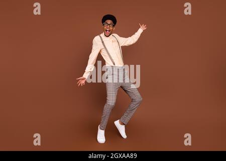 Photo of funky positive guy dance crazy moves wear suspenders sneakers isolated brown color background. Stock Photo