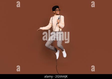 Full length body size view of attractive cheerful funny guy jumping singing hit isolated over brown color background. Stock Photo