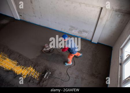 Laborer performing and polishing sand and cement screed floor on the construction site of a new two-level apartment. Sand and cement floor screed Stock Photo