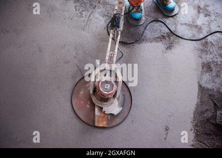 Laborer performing and polishing sand and cement screed floor on the construction site of a new two-level apartment. Sand and cement floor screed Stock Photo