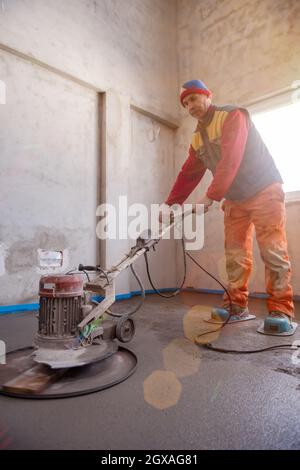 Laborer performing and polishing sand and cement screed floor on the construction site of a new two-level apartment. Sand and cement floor screed Stock Photo