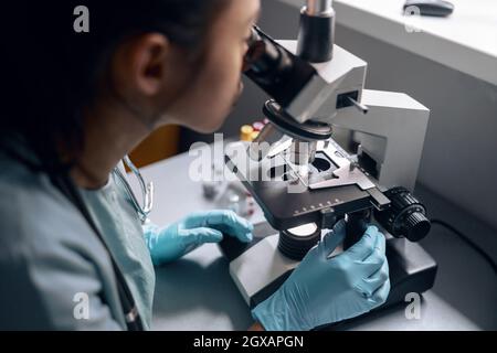 Young worker works with microscope researching material at table in laboratory Stock Photo