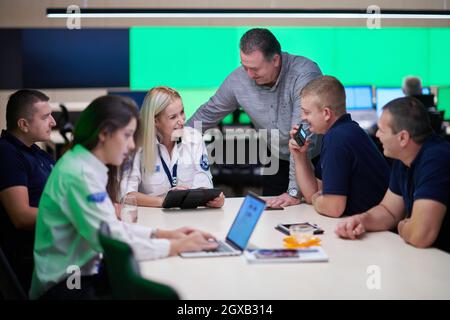Group of security guards sitting and having briefing In the system control room  They're working in security data center surrounded by multiple Screen Stock Photo
