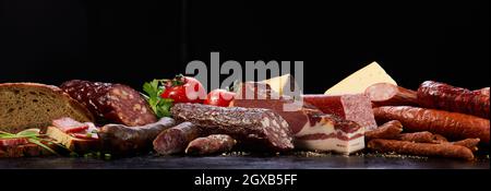 Assorted types of cured sausages neat bread placed on dark surface with vegetable and cheese in studio on black background Stock Photo