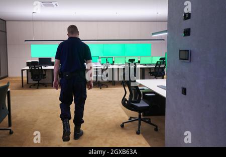 young male security operator walking through data system control room Working at workstation with multiple displays, security guard working on multipl Stock Photo
