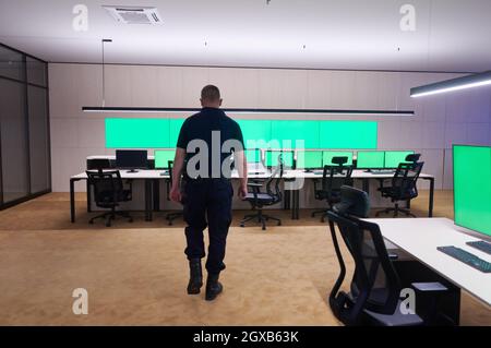 young male security operator walking through data system control room Working at workstation with multiple displays, security guard working on multipl Stock Photo