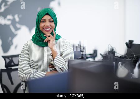 Portrait of muslim african female software developer with green hijab standing at modern open plan startup office Stock Photo