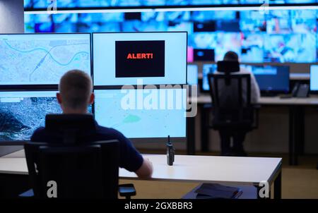 Male security operator working in a data system control room offices Technical Operator Working at  workstation with multiple displays, security guard Stock Photo