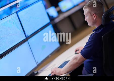 Male security operator working in a data system control room offices Technical Operator Working at  workstation with multiple displays, security guard Stock Photo