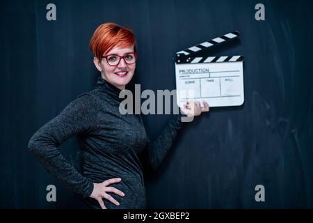 redhead woman on black chalkboard holding movie clapper cinema concept Stock Photo